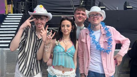 From left, Lennon, Jess, Ryan and Sam smile into the camera as they stand in front of one of the event's stages. They are dressed up with two of the boys wearing cowboy hats.
