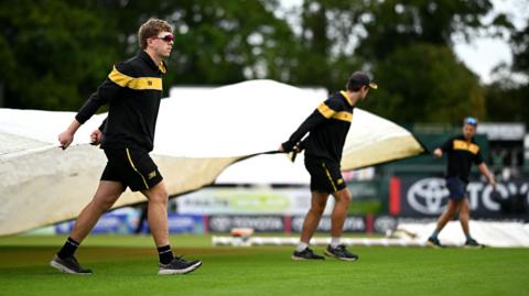 Groundstaff cover the pitch during a rain delay