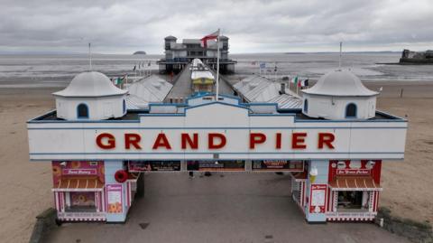 The front of the Grand Pier in Weston with the pier stretching out behind into the sea, and Grand Pier in big red letters.