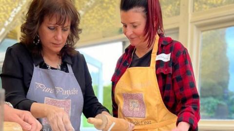 Surinder Hothi is showing another woman something just out of shot. They are both looking down onto a work surface.