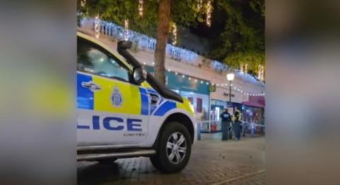 A police car is parked outside a shop at night. Christmas decorations are visible. 