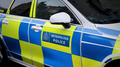 A police car with a Metropolitan Police log and blue and yellow chequerboard pattern on the side 