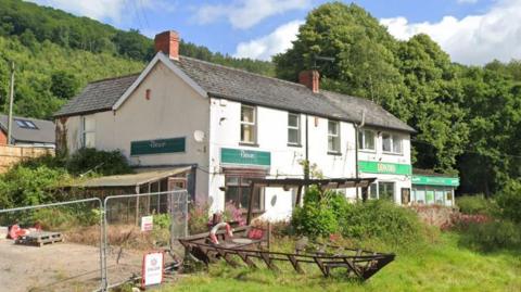 A vacant white-painted shop called Browns General Stores with a patch of untidy land next to it. Next door is a Londis shop