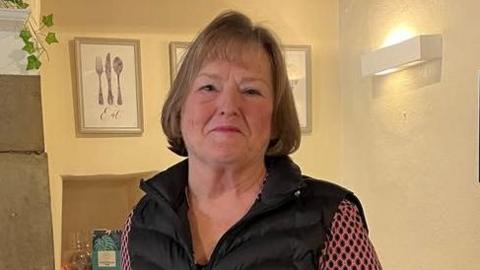 Elsie Whitehead has short brown hair and is wearing a dark sleeveless jacket.