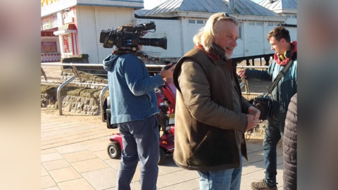 Presenter Henry Cole in Weston-super-Mare with a television crew behind him.