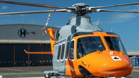 A yellow and grey helicopter in front of a HeliOperations base.