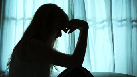 Silhouette of woman sitting in bed by window