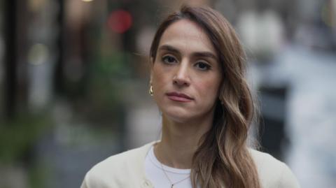 Mahsa Alimardani, a woman with long hair over her shoulder, stands in a street