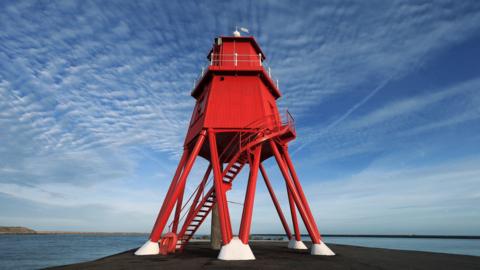 Herd Groyne lighthouse, looking resplendent in red, on a sunny day.