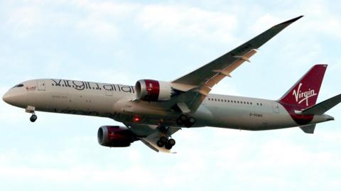 A large white passenger plane in flight. It carries red Virgin Atlantic branding.