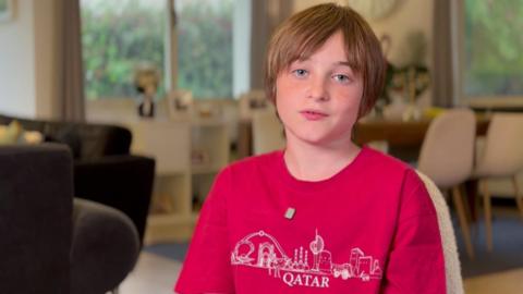 Boy sat with a red t-shirt on talking to the camera