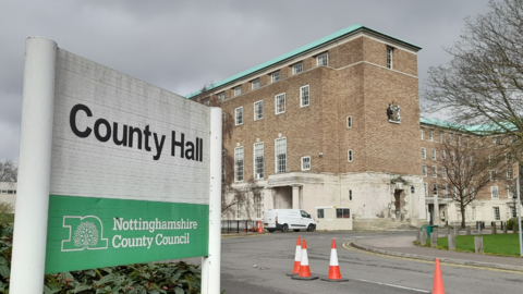 County Hall is pictured. It is a multi-storey brick building. To the left is a sign which says "County Hall Nottinghamshire County Council"