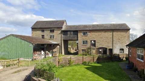 A old stone building made of a three-storey building connected to a four-storey building via a wooden-clad bridge