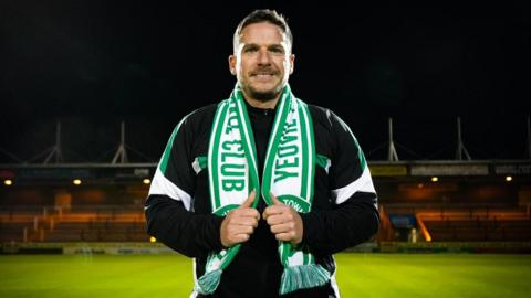 Billy Rowley standing at Huish Park on the pitch wearing a Yeovil scarf around his neck