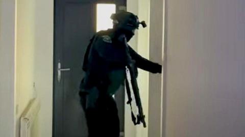 A screengrab from a video shows an armed police officer searching a house