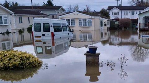 A residential area is flooded. A few houses and vans are partially submerged in the water.