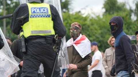 A police officer stands in front of two masked men