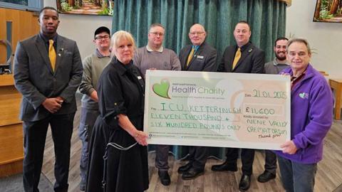 A group of people display a large novelty cheque for £11,600 in a crematorium.