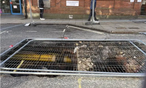 A grey road with a large sinkhole in the middle of it, covered by a metal grey fence