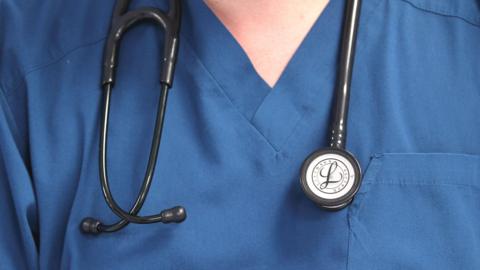 A close up of a doctor's scrubs. They are blue and the doctor has a stethoscope around their neck. 
