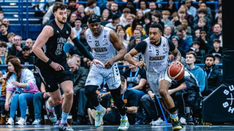 Ray'Sean Taylor (3, right) prepares to bounce the ball in his left hand for Newcastle Eagles as team-mate Emmanuel Kanwei (21) watches on (centre) and London Lions player Ethan Price (10) tries to get close. Newcastle players in white, London player is in all black.