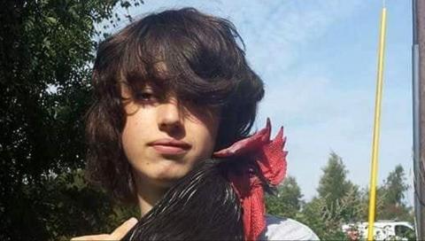 A young man with long brown hair holds a chicken