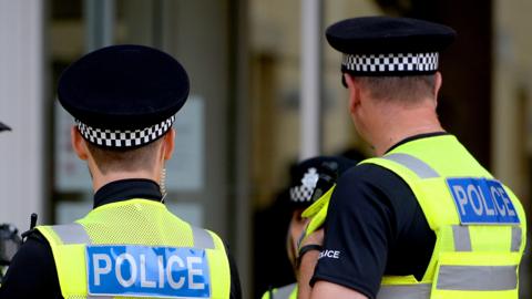 Two police officers stand with their back to the camera in uniform