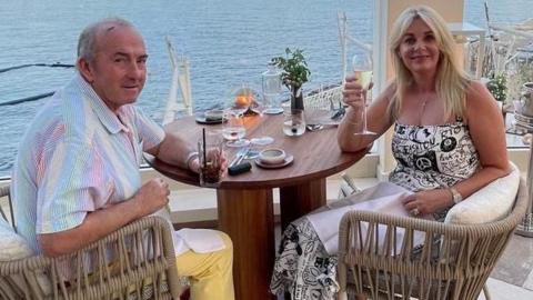 Rick and Rachel Oakes pose for a photo while on holiday. Mr Oakes has short grey hair, while Mrs Oakes has medium-length blonde hair.