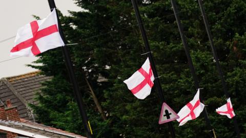 A row of four black lampposts with a small England flag tied to each.