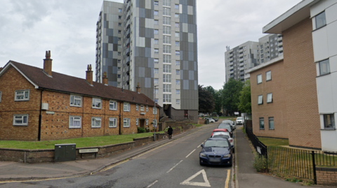 Bailey Street in Luton. Terraced houses, parked cars and tower blocks in the background can be seen