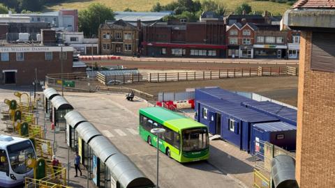 A view over the bus stop at Glovers Walk in Yeovil. A green bus is parked by the stop.