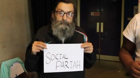Man holding up card saying "social pariah"