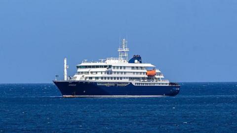 The blue and white cruise ship MV Hondius stationary in the ocean off the port of Praia, the capital of Cape Verde.