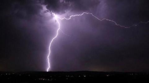 A bright shaft of lightning striking ground illuminates a dark night sky