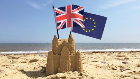 A sandcastle on a beach with a British and an EU flag in it