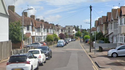 A shot of a street in Southend. There are 1950s-style terraced houses on either side. Cars are parked in the street.