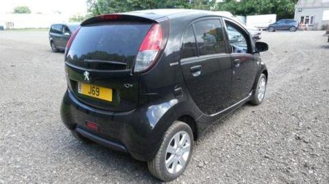 A midshot of the Peugeot Ion facing away. It is black, and has a number plate with J69 on it.