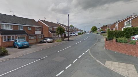 Streetview picture of the road showing brick-built houses with cars in the drive.