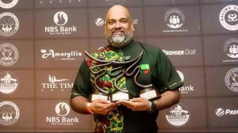 Arjun Menon holds up an award at a Malawi sports event