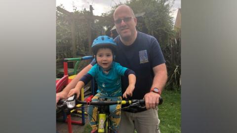 Simon Lambert stands above Archie, who is sat on a bicycle