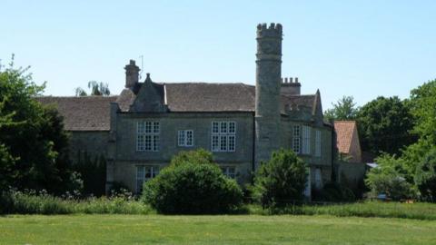 Grade II listed building with tall chimney and fronted by fields