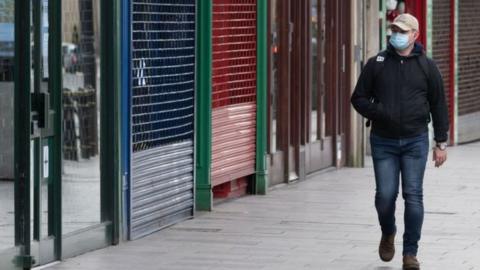 Man walking passed closed shops