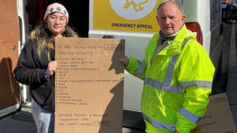 Kev Draper with a volunteer holding up a sign with items needed