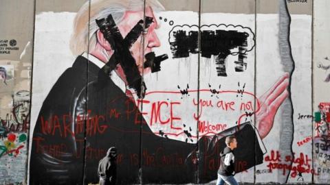 Palestinian children walk past vandalised graffiti depicting US President Donald Trump and slogans saying US Vice-President Mike Pence is "not welcome" in Bethlehem, West Bank. Photo: 7 December 2017