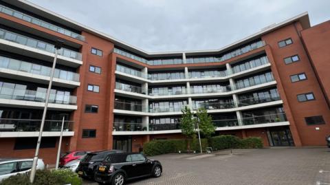 The image shows Chatham House. It has white balconies in rows with red brick work either side. 