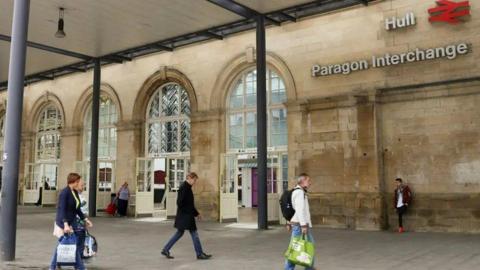 A stock image of the outside of Hull Paragon station with people carrying shopping bags and walking past