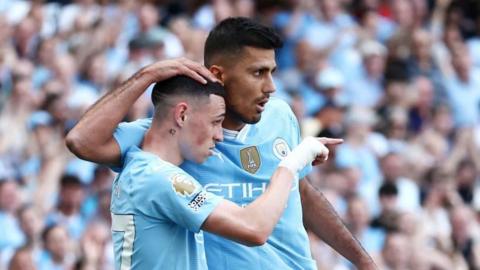 Manchester City players Phil Foden and Rodri. Rodri has his arm around Foden and a hand on his head 