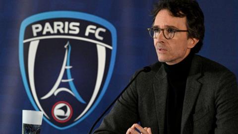 Antoine Arnault sits by a microphone in front of a large Paris FC club crest