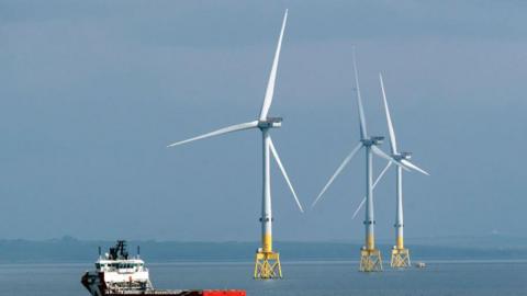 A wind farm off the coast of Aberdeen Three wind turbines on the water spin, while a small ferry sails past nearby 