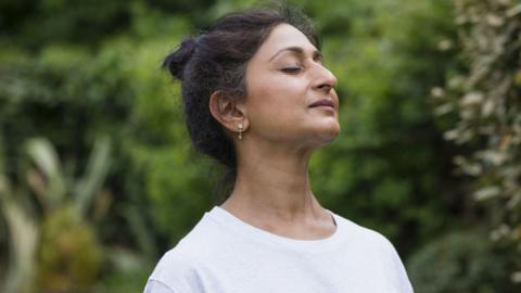 Someone with their eyes closed looking calm. There are trees in the background.